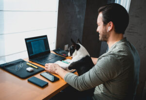 man working remote on a laptop with a dog on his lap